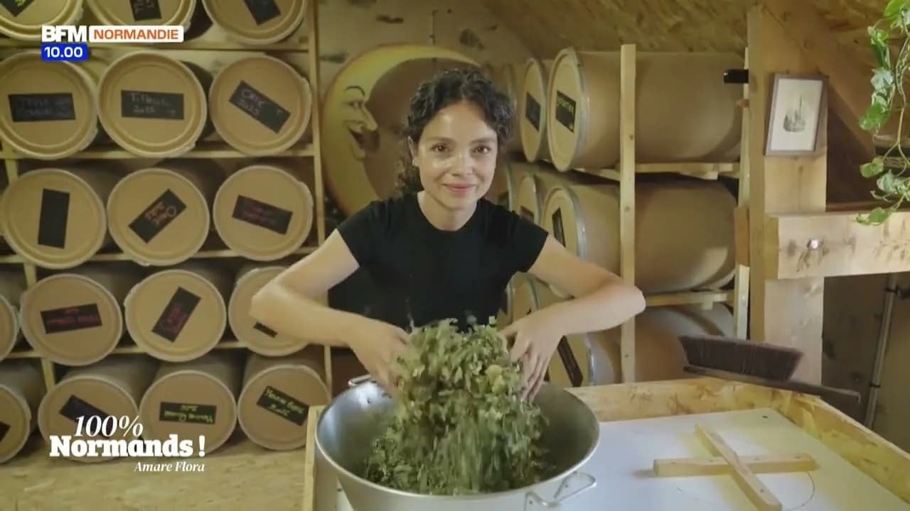 Alexandra Chennevière dans son séchoir, les bras dans une bassine de plantes séchées, devant les rangées de tambours de séchage